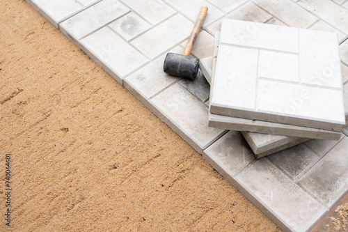 Scene of an ongoing pavement or tile installation. There is a rubber mallet and tiles on top of the partially completed pavement, indicating that the work is in progress.