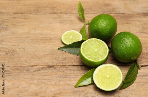 Fresh limes and leaves on wooden table. Space for text