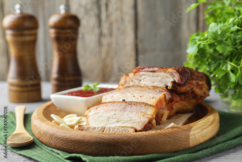 Pieces of baked pork belly served with sauce on grey wooden table, closeup
