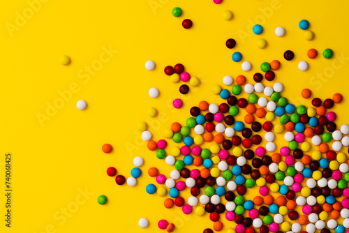 Colorful chocolate beans on yellow background.