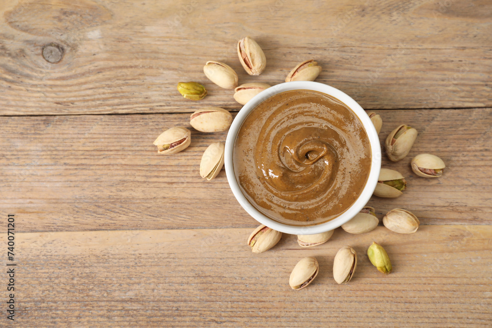 Delicious nut butter in bowl and pistachios on wooden table, top view. Space for text Delicious nut butter in bowl and pistachios on wooden table, top view. Space for text