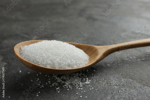 Spoon with granulated sugar on grey textured table, closeup