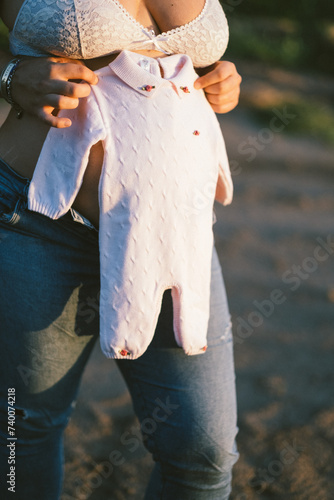 Sección baja de mujer embarazada sosteniendo vestimenta de bebé photo