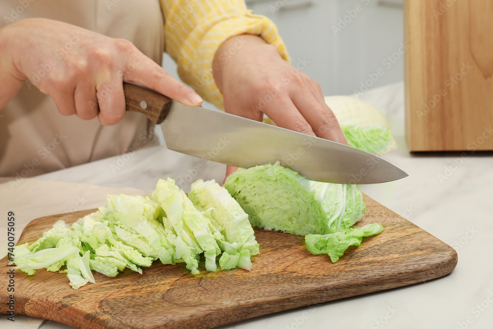 Woman cutting fresh chinese cabbage at table in kitchen, closeup Woman cutting fresh chinese cabbage at table in kitchen, closeup