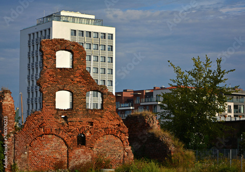 ruiny budynku z oknami oświetlone słońcem, ceglana ściana z oknami na tle nowoczesnego budynku, brick walls with window openings of a ruined house on the background modern building,