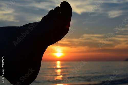 stopa i zachód słońca nad morzem, relaks na plaży o zachodzie słońca, foot, relaxing on the beach at sunset, foot against the background of the setting sun, vacation 