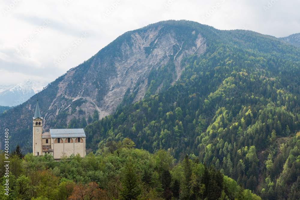 Small church on the hill in Dolomites mountains, Belluno, Veneto, Italy. Chiesa Parrocchiale di San Martino in Italian Alps in a cloudy day at springtime