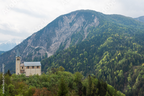 Small church on the hill in Dolomites mountains, Belluno, Veneto, Italy. Chiesa Parrocchiale di San Martino in Italian Alps in a cloudy day at springtime