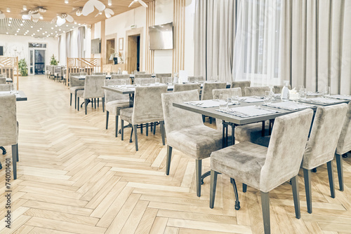 Side view of a large empty bright restaurant with tables, soft chairs, curtains and a wooden floor. Modern interior of a cafe, restaurant for events, holidays, weddings, birthdays with copy space.