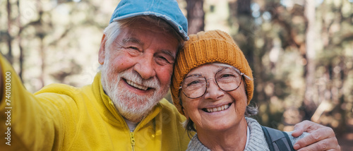 Head shot portrait close up of cute couple of old seniors taking a selfie together in the mountain forest looking at the camera smiling having fun enjoying. Two mature people hiking.