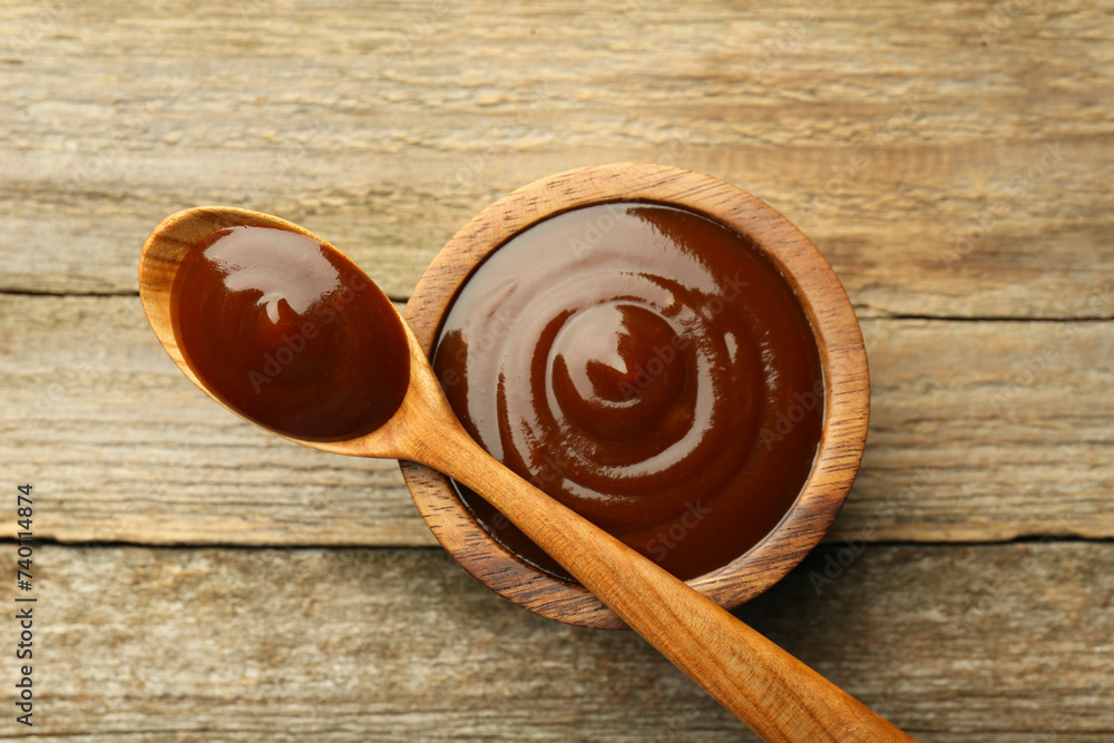 Tasty barbeque sauce in bowl and spoon on wooden table, top view Tasty barbeque sauce in bowl and spoon on wooden table, top view