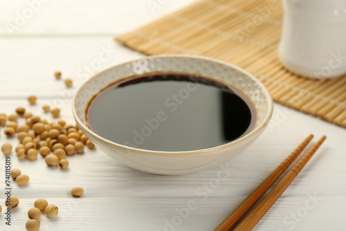 Cuadro en lienzo Tasty soy sauce in bowl, chopsticks and soybeans on white wooden table, closeup