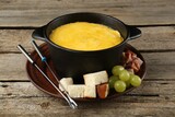 Fondue pot with melted cheese and different products on wooden table