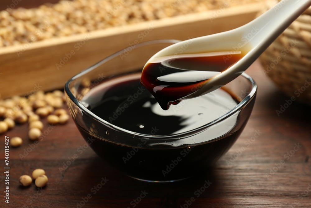 Taking soy sauce with spoon from bowl at wooden table, closeup Taking soy sauce with spoon from bowl at wooden table, closeup
