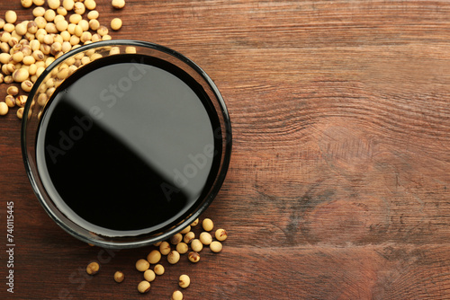 Soy sauce in bowl and soybeans on wooden table, flat lay. Space for text