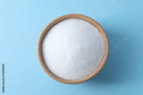 Organic white salt in bowl on light blue background, top view