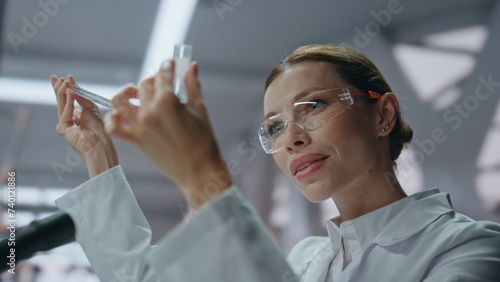 Smiling microbiologist examining test tube with medicines in laboratory closeup.