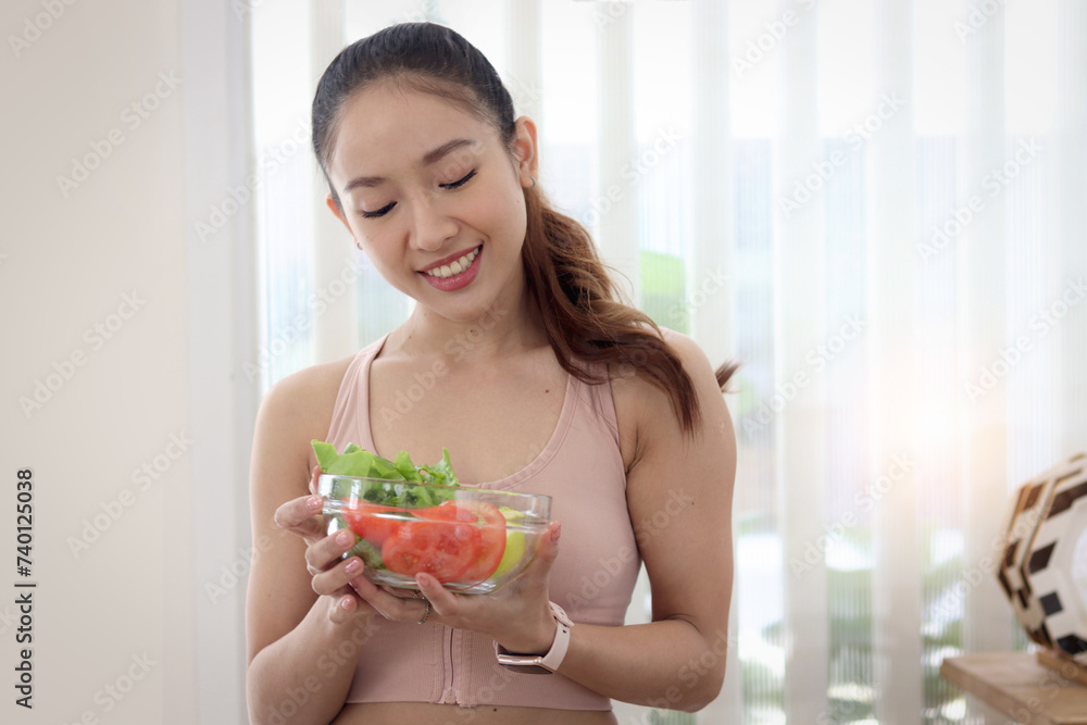 Sporty girl in fitness sport wear holding salad bowl, Beautiful happy smiling Asian woman in kitchen eating vegetable salad for healthy, losing weight and slim. Healthy food fitness workout Sporty girl in fitness sport wear holding salad bowl, Beautiful happy smiling Asian woman in kitchen eating vegetable salad for healthy, losing weight and slim. Healthy food fitness workout