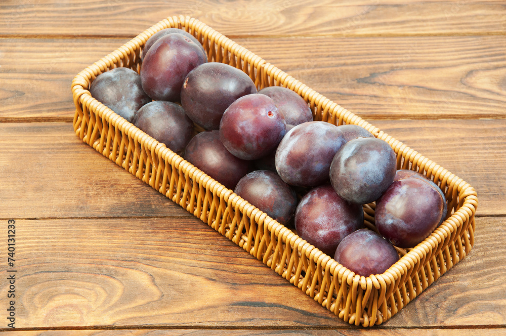 round blue plums in a basket on a wooden background. ripe sweet plums on a table