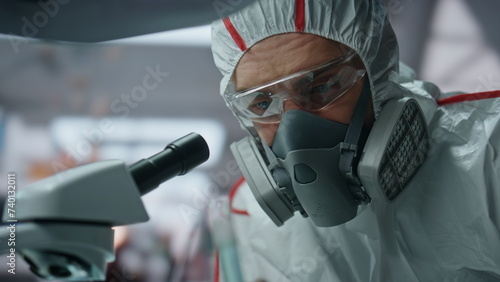 Biochemistry specialist looking microscope in decontamination suit lab close up photo