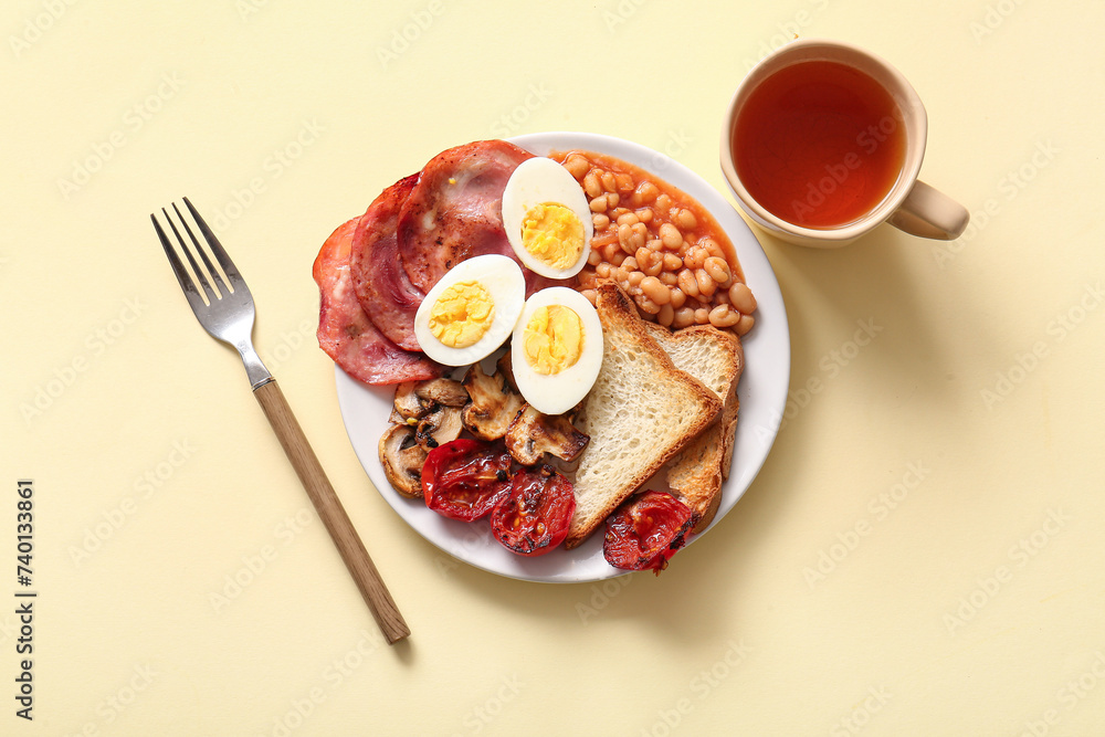Plate with tasty English breakfast and cup of tea on yellow background