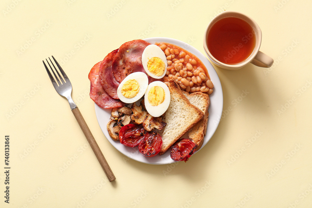 Plate with tasty English breakfast and cup of tea on yellow background Plate with tasty English breakfast and cup of tea on yellow background