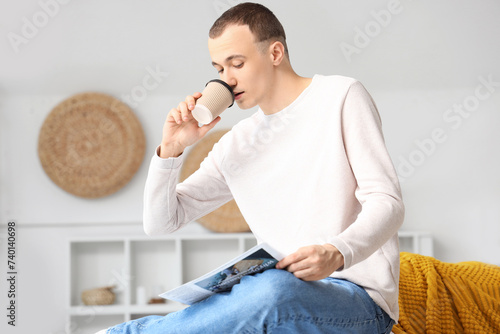 Young man with newspaper drinking coffee at home