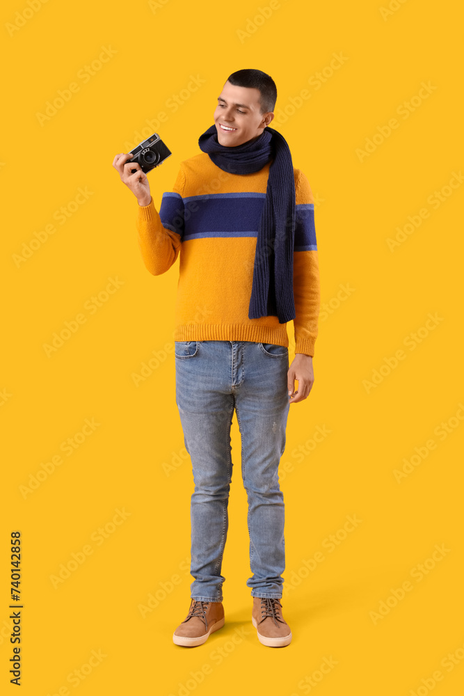 Young man in winter clothes with photo camera on yellow background Young man in winter clothes with photo camera on yellow background