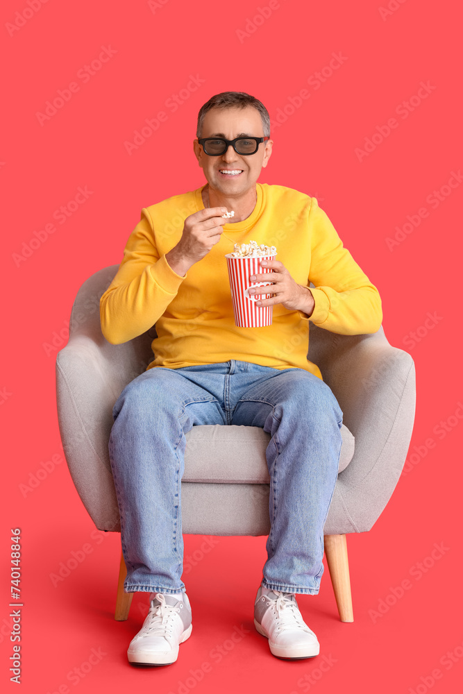 Mature man with 3D glasses and popcorn watching movie in armchair on red background Mature man with 3D glasses and popcorn watching movie in armchair on red background
