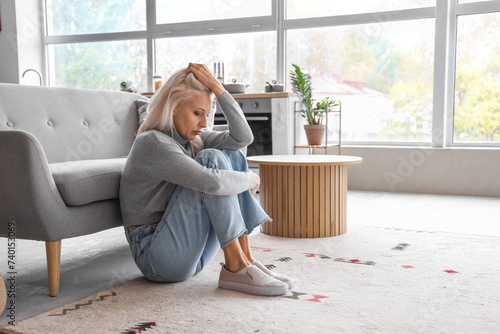 Depressed mature woman sitting on floor at home photo