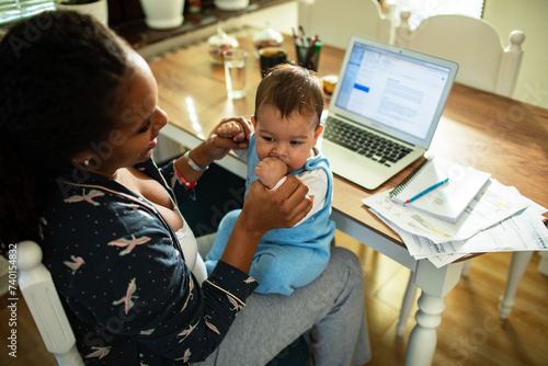 Multitasking mother holding baby while working from home photo