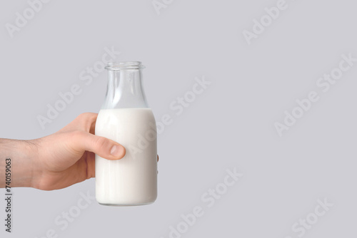 Hand with bottle of milk on grey background