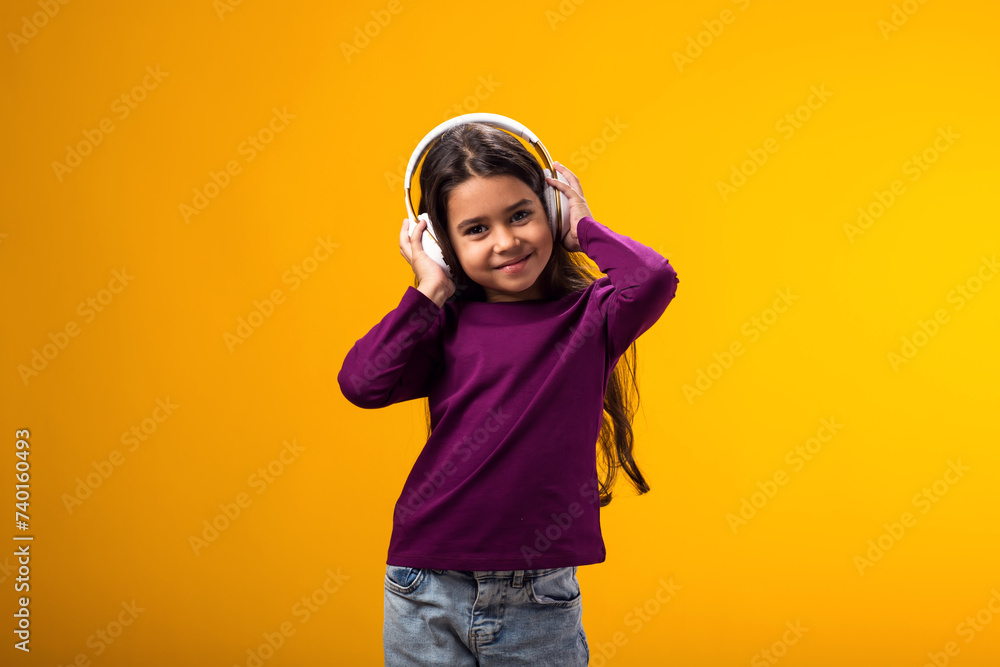 Smiling kid girl enjoying music in headphones on yellow background. Lifestyle and leasure concept Smiling kid girl enjoying music in headphones on yellow background. Lifestyle and leasure concept