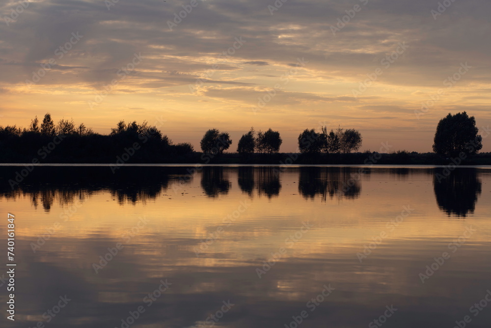 View of the lake in twilight. Sunset, warm colors. Calm water reflecting clouds.