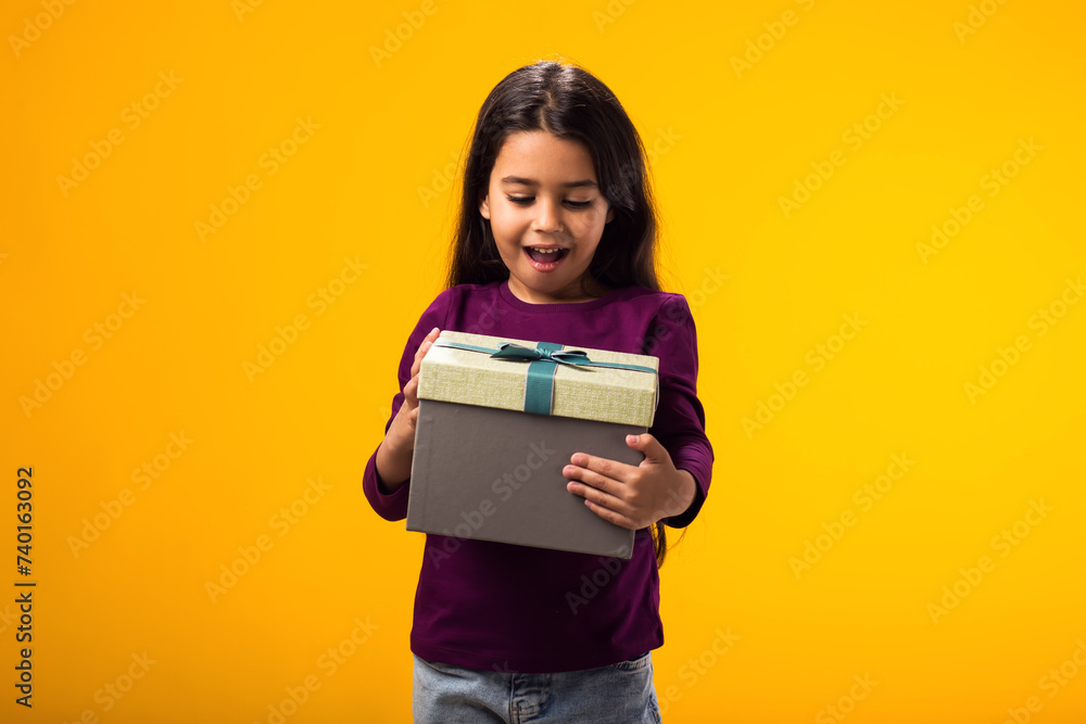 Surprised kid girl holding giftbox over yellow background. Birthday and celebration concept Surprised kid girl holding giftbox over yellow background. Birthday and celebration concept