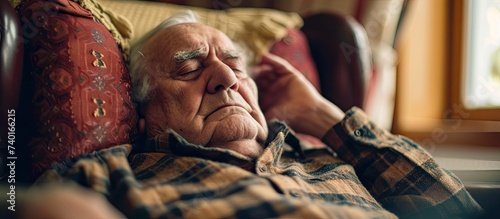 An elderly man reclining on a couch with his eyes closed, peacefully taking a nap.