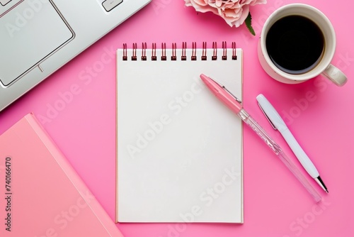 Vibrant pink-themed workspace with laptop, notepad, pen, and a cup of coffee. lively office setting with technology, writing supplies, and a hot drink, all laid out on a pink surface