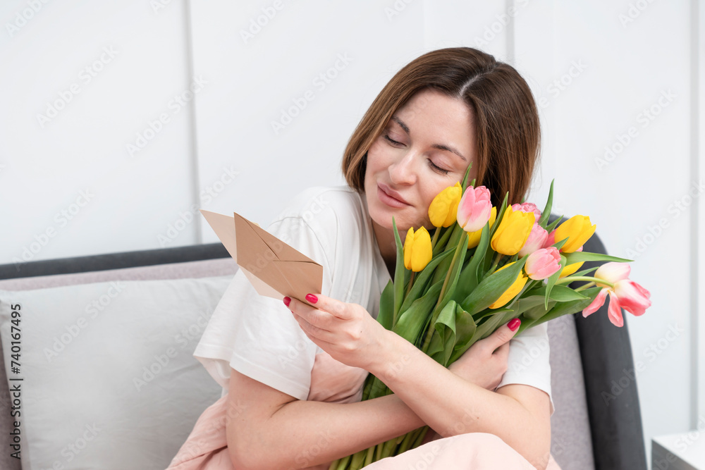 A young beautiful girl received a bouquet of flowers and a congratulatory letter on a wonderful World Women's Day. She sits and reads the letter and thanks the sender A young beautiful girl received a bouquet of flowers and a congratulatory letter on a wonderful World Women's Day. She sits and reads the letter and thanks the sender