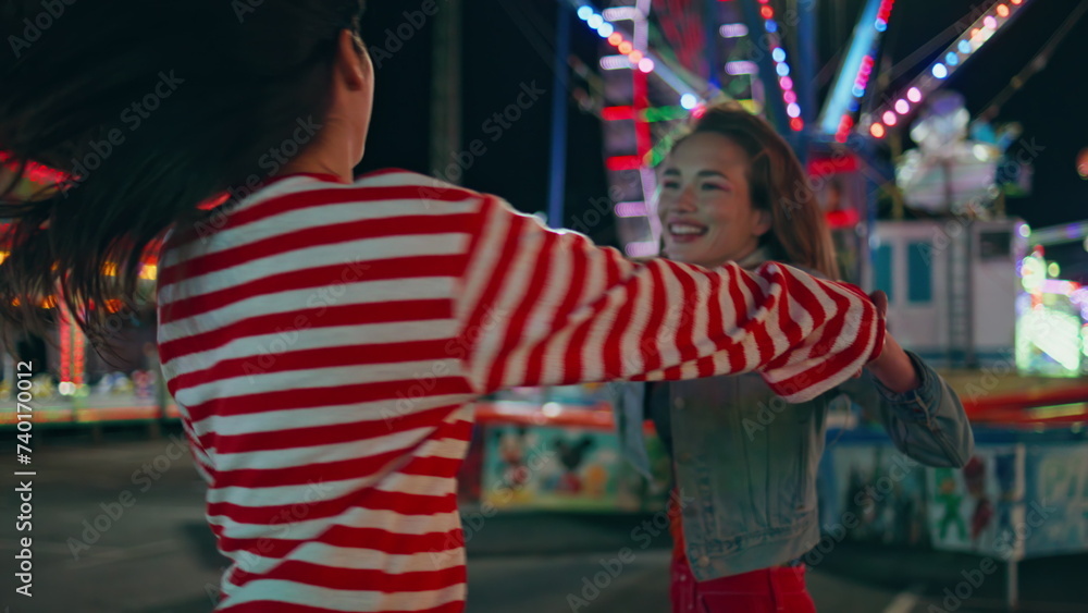 Naklejka premium Closeup happy girls dance city funfair at night. Cheerful best friends have fun