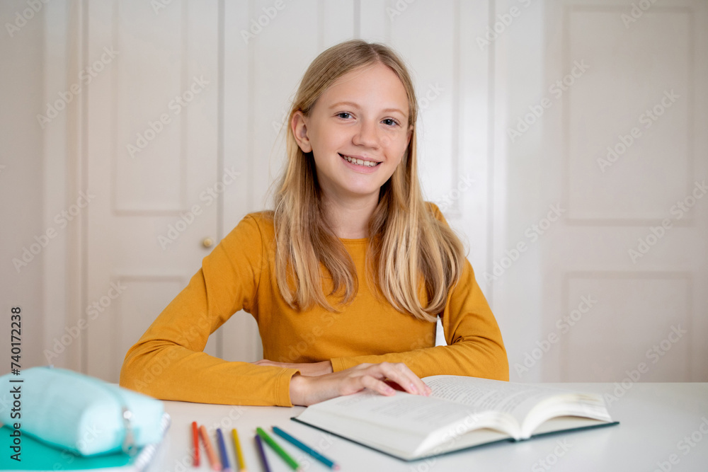 Smiling teenage girl sitting at desk with an open book at home Smiling teenage girl sitting at desk with an open book at home