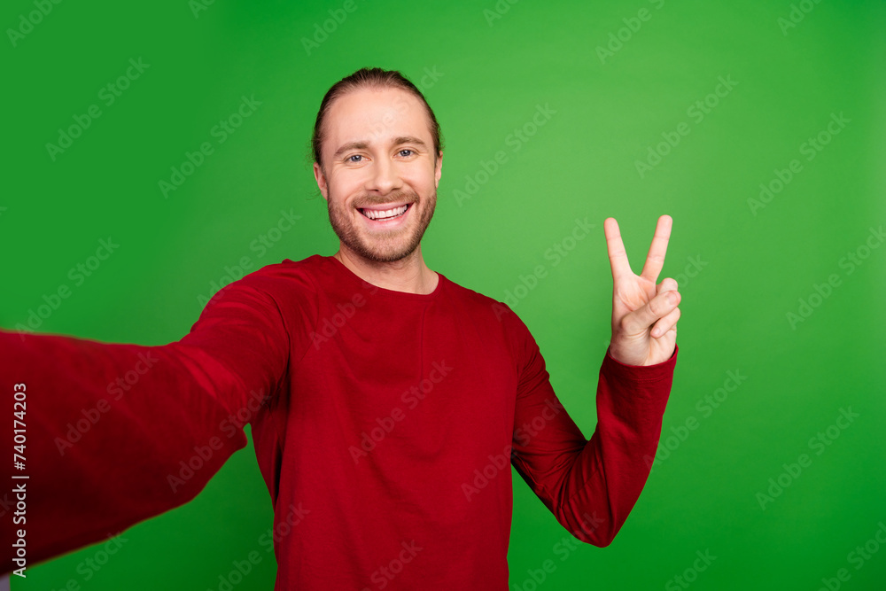 Photo of cheerful nice man with stubble long hairdo dressed red pullover showing v-sign make selfie isolated on green color background Photo of cheerful nice man with stubble long hairdo dressed red pullover showing v-sign make selfie isolated on green color background