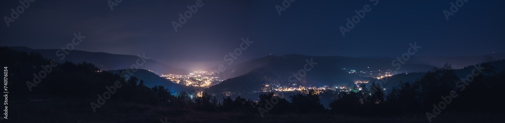 A small glowing city with houses surrounded by mountains. dark blue purple starry night