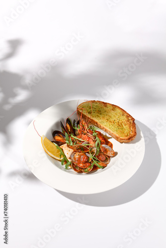 Sautéed shellfish medley with ciabatta toast, side view on white plate with leaf shadow art