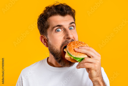 funny guy satisfying food cravings with cheeseburger on yellow background