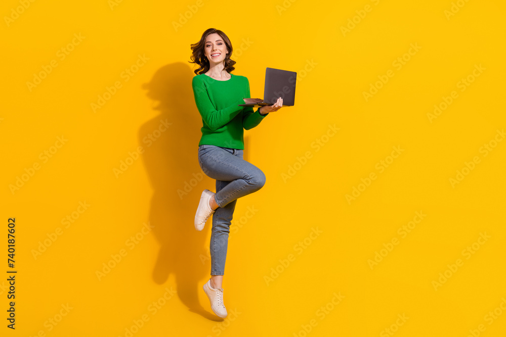 Full body size photo of young girl work using laptop jumping hold laptop shopaholic order xmas gifts isolated on yellow color background Full body size photo of young girl work using laptop jumping hold laptop shopaholic order xmas gifts isolated on yellow color background