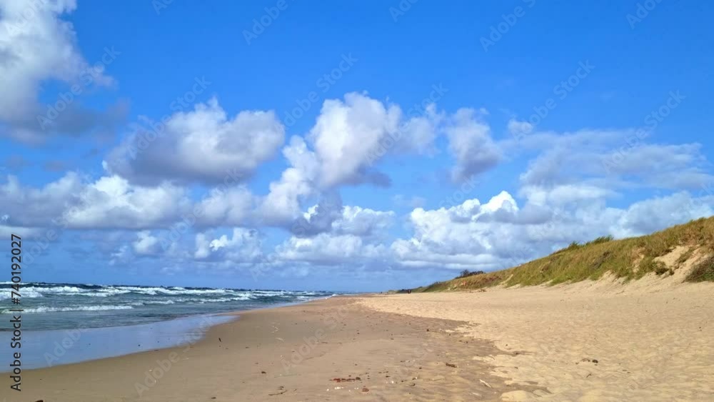 A sandy beach stretches along the shore, meeting the oceans waves under a cloudy blue sky. The waves crash against the shore, creating a soothing sound as seagulls fly overhead. Footprints mark the sa A sandy beach stretches along the shore, meeting the oceans waves under a cloudy blue sky. The waves crash against the shore, creating a soothing sound as seagulls fly overhead. Footprints mark the sa