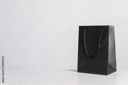 Black paper bag on white wooden table, space for text