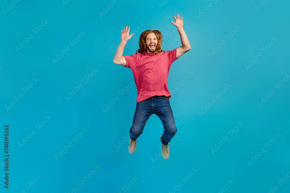 Full body portrait of astonished active person jumping raise arms empty space isolated on blue color background Full body portrait of astonished active person jumping raise arms empty space isolated on blue color background
