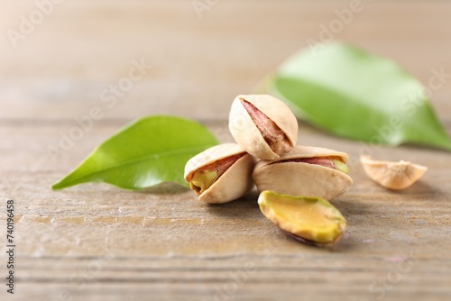 Tasty pistachios and leaves on wooden table, closeup. Space for text