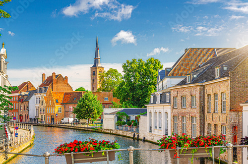 Bruges cityscape, Sint Annarei water canal, houses buildings on promenade in Brugge old town, flowers pots on fence, Bruges city historical centre, Saint Anna Church tower, Flemish Region, Belgium photo